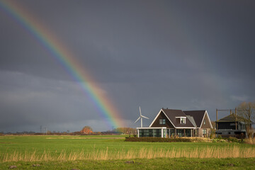 Holenderska farma, uroczy domek wśród pól, w tle zachmurzone niebo z tęczą. - obrazy, fototapety, plakaty