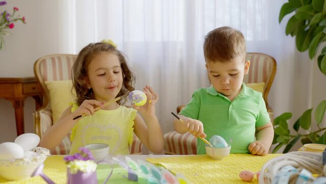 Cute little kids preschooler enjoy painting eggs for easter, smiling joyfully. Little girl and little boy having fun. Sister and Brother painting together.