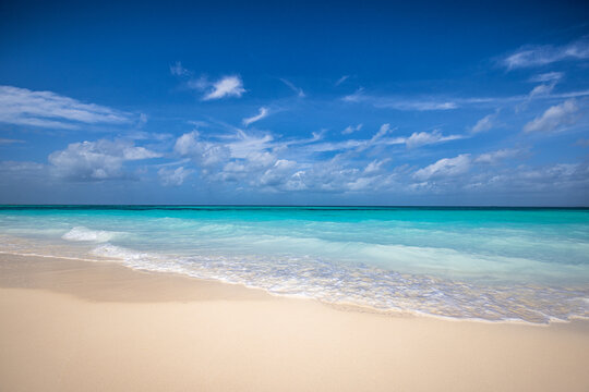 Closeup sandy beach waves and blue summer sky. Panoramic beach landscape. Empty tropical beach and seascape, horizon. Bright blue sky, soft sand, calmness, tranquil seaside relaxing sunlight, summer 