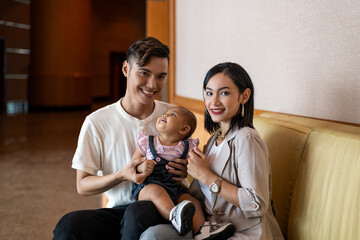 Malay Asian Young Couple with One Year Old Child Daughter, with light brown sofa chair - obrazy, fototapety, plakaty