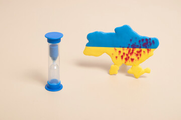 Fototapeta premium Hourglass.and plasticine yellow and blue map of Ukraine with shots and blood. Stop the war concept