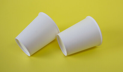 Two small white paper cups on a yellow background