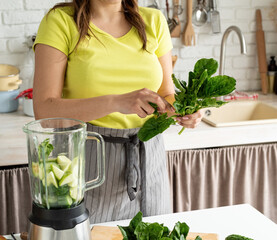 Young woman making green spinach smoothie at home kitchen