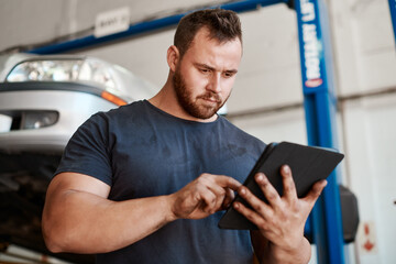 Open the app to find a reliable and trustworthy mechanic near you. Shot of a mechanic using a digital tablet while working in an auto repair shop.