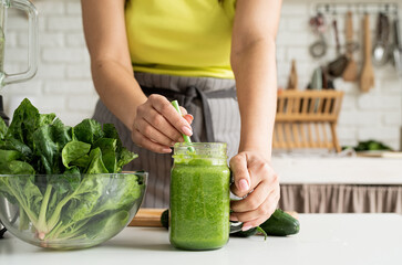 Close up of a young woman holding a jar of green smoothie