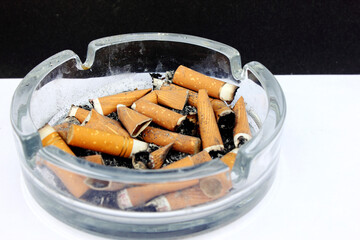 Lots of dirty used cigarette butts in the ashtray. Glass ashtray. Health, smoking, harm to health, Cancer of the lungs. Copy space for text