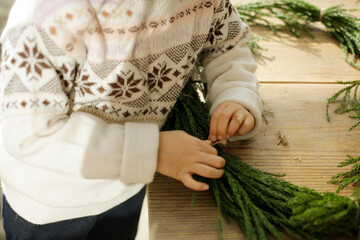 girl making cedar wreath on wooden craft table. child tying a knot.