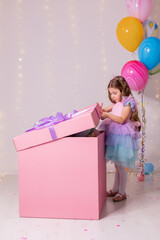 charming little girl in a beautiful dress opens a huge pink box with a surprise. child receives a birthday present. balloons in a box. lifestyle. space for text. High quality photo