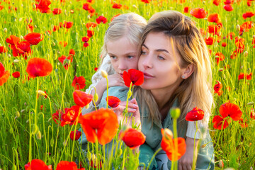 Obraz na płótnie Canvas Beautiful mother and daughter in spring poppy flower field. Mom holds her child daughter in the flowering meadow. Spring design.