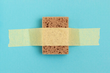 Dishwashing sponge glued with adhesive tape on a blue background.