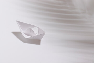 Paper boat on a white background. Hard shadow. High angle view.