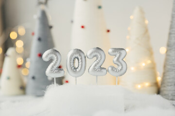 Silver number 2023 on nandmade Christmas trees background. Yarn wrapped cone trees and garland on background
