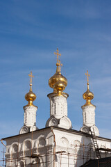 Fototapeta na wymiar Three golden orthodox bright crosses are on top of golden cupolas on the top of the stone white under construction church against blue dark sky