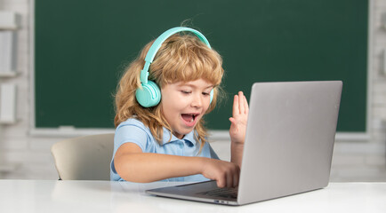 Small boy in headphones watch video lesson on computer in school, child in earphones have online lesson, using laptop. Remote study and education.