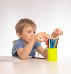 Cute little boy with blonde hair draws at a table, white background