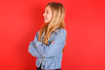 blonde little kid girl wearing denim jacket over red background cross hands look copy space