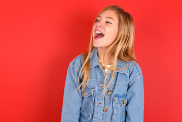 blonde little kid girl wearing denim jacket over red background very happy and excited about new...