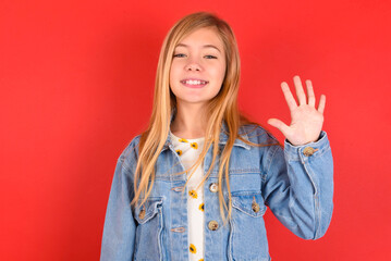 blonde little kid girl wearing denim jacket over red background showing and pointing up with fingers number five while smiling confident and happy.
