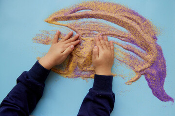 Baby plays with colorful sand. Child fine motor skills development. Creative kids occupation. View...