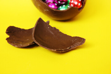 A cracked chocolate Easter egg with colorful little round candies inside. Happy Easter. Chocolate. Sweets for children and adults. Candy. Dessert. Copy space. Top view. Flat lay