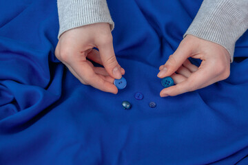The girl selects buttons matching the color of the blue fabric. Hobby, sewing.
