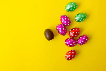 Chocolate egg in colorful foil for Easter on yellow background. The egg is wrapped in red foil. Happy Easter. Chocolate. Sweets for children and adults. Candy. Dessert. Copy space. Top view. Flat lay