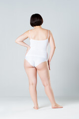 Fat woman in underwear on gray background, cellulite on female body