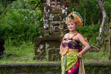 Portrait Balinese dancer woman at old temple with traditional peacock costume