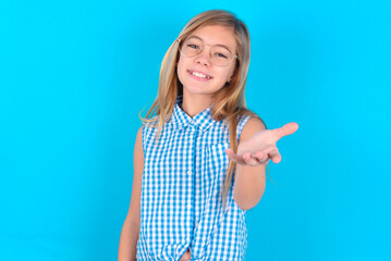 little kid girl with glasses wearing plaid shirt over blue background smiling friendly offering something with open hand or handshake as greeting and welcoming. Successful business.