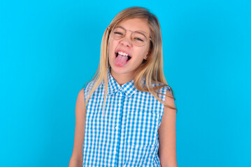 little kid girl with glasses wearing plaid shirt over blue background  with happy and funny face...