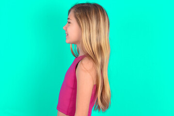 Profile of smiling blonde little kid girl wearing pink sport clothes over green background with...