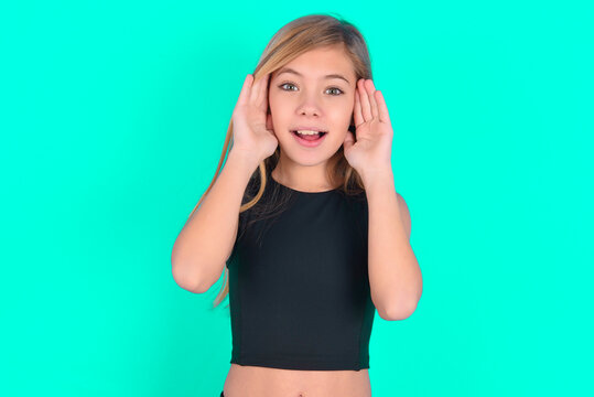 blonde little kid girl wearing black sport clothes over green background Pleasant looking cheerful, Happy reaction