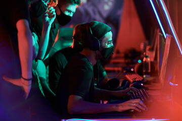 Group of young gamers in facial masks supporting leader while he participating in esports tournament