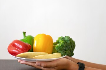 A picture of hands of a woman holding plate full of healthy exotic vegetables such as broccoli,...