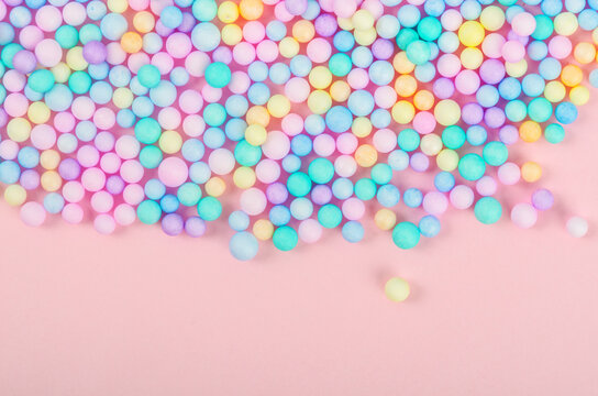 Foam beads of various colors brightly colored on pink pastel background.