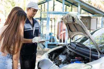 Fototapeta na wymiar Asian male auto mechanic holds a clipboard and examines car engine breakdown problem with women customer and explain the root cause and estimate repair quotation, Car repair, and maintenance concept.