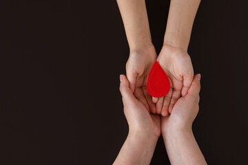 World hemophilia day. Hands of mother and baby hold drop of blood on black background. Concept of...
