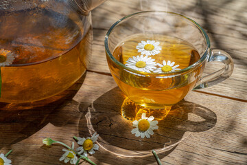 Glass of herbal chamomile tea and chamomile flowers on old wooden table. Close-up.