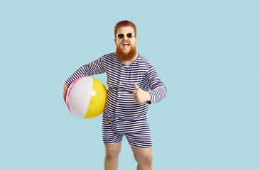 Funny cheerful chubby guy holds beach inflatable ball and shows thumb up on pastel turquoise...