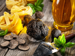 Black edible winter truffle, tagliatelle and fresh basil on wooden table. The most popular cooking...