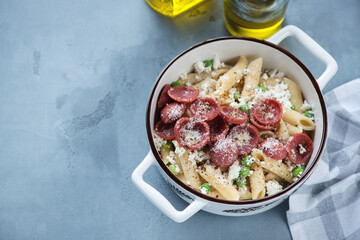 Crispy salami, crushed green pea and ricotta pasta in a white serving pan, high angle view on a grey concrete background, horizontal shot, copyspace