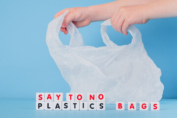 Say no plastics bags words from cubes on the background of children's hands holding a plastic bag. Plastic free concept.