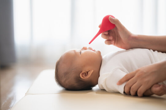 mother cleaning the nose of a newborn baby with nasal aspirator or syringe ball