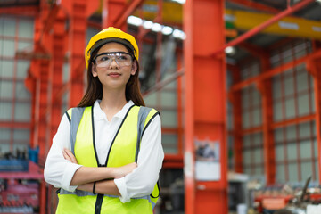 Portrait of Young female engineer in safety vest and glasses with yellow helmet standing arms...