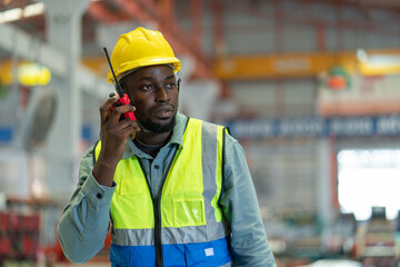 Male black worker wear safety vest with yellow helmet using walkie-talkie to command tasks while...