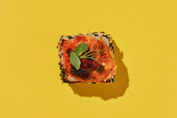Hot baked suchi roll with salmon on yellow background.
