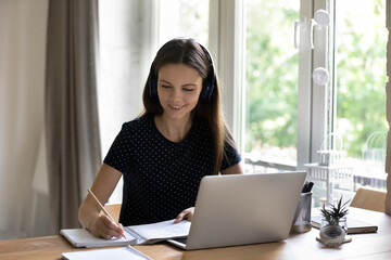 Diligent student in headphones makes task sit at desk with laptop, e-learn english, take part in...