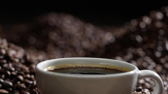 Drop of coffee falling into coffee cup sitting in a pile of freshly roasted coffee beans. Slow motion.