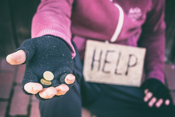 Bettelnde Hand mit einzelnen Münzen und Pappschild mit der Aufschrift Help