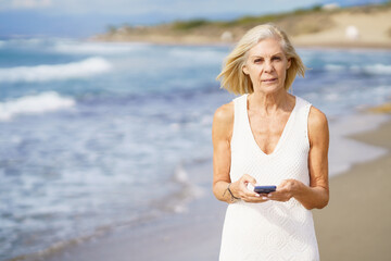 Fototapeta na wymiar Mature woman walking on the beach using a smartphone.